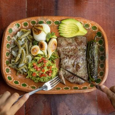 Authentic Mexican meal featuring grilled steak, avocado, and vegetables on a ceramic plate.