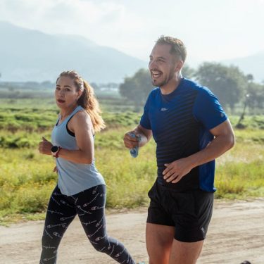 Two adults running on a rural dirt path, enjoying a sunny day outdoors.