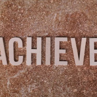 Wooden letters spelling 'ACHIEVE' on a textured brown surface, conveying motivation and success.